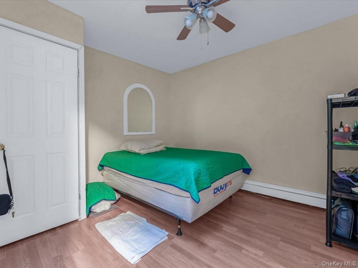 Bedroom with wood finished floors, a baseboard heating unit, and ceiling fan