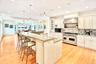Chefs Kitchen featuring backsplash, Viking range with two ovens, a spacious island, light stone counters, and wall chimney exhaust hood.