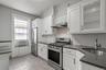 Kitchen featuring stainless steel appliances, white cabinetry, light wood-type flooring, under cabinet range hood, and dark stone counters