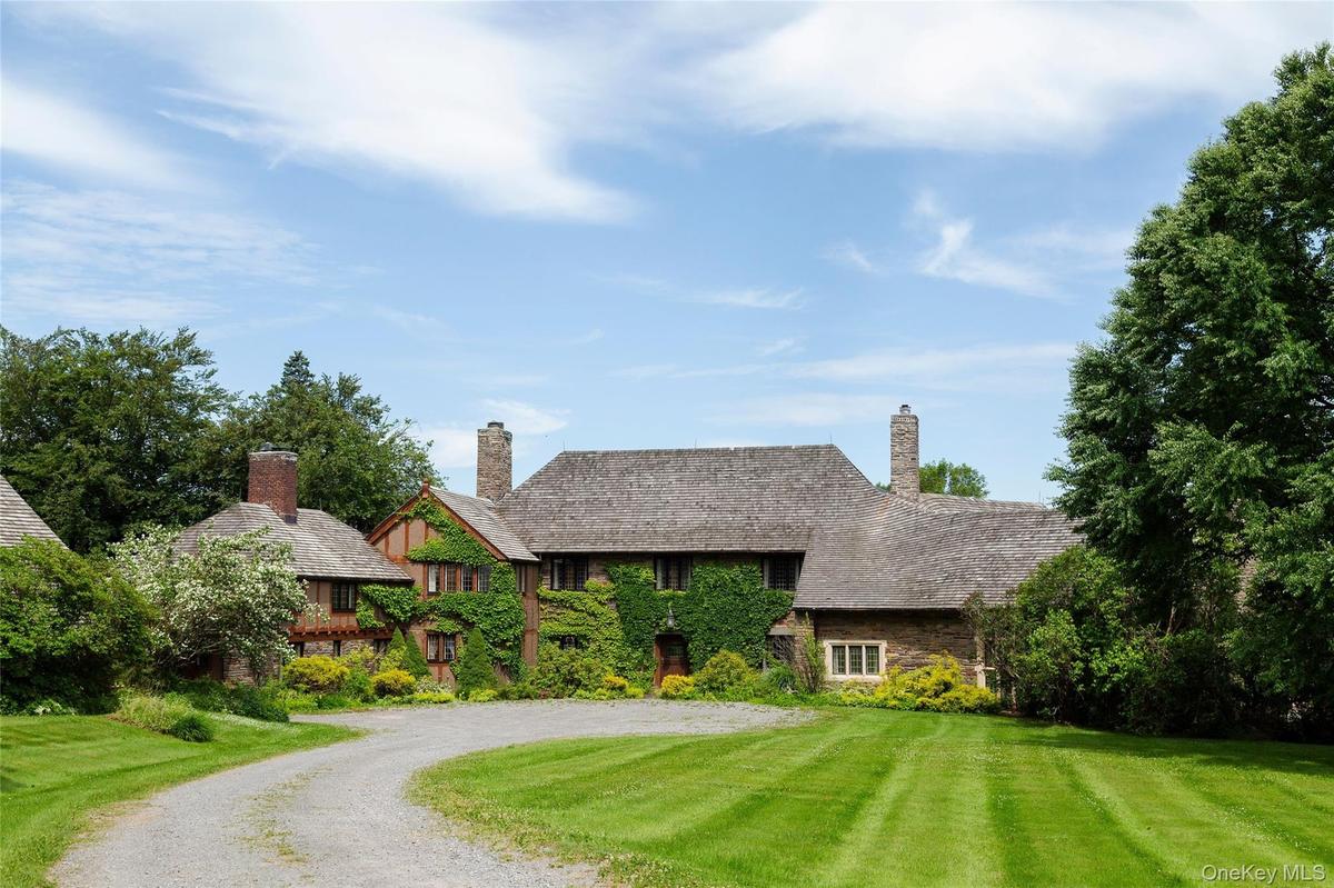 Tudor-style house with a chimney, a front lawn, driveway, and stone siding