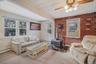 Carpeted living room with brick wall, a wood stove, a baseboard radiator, and ceiling fan
