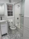Full bath featuring tile walls, combined bath / shower with glass door, wainscoting, and vanity