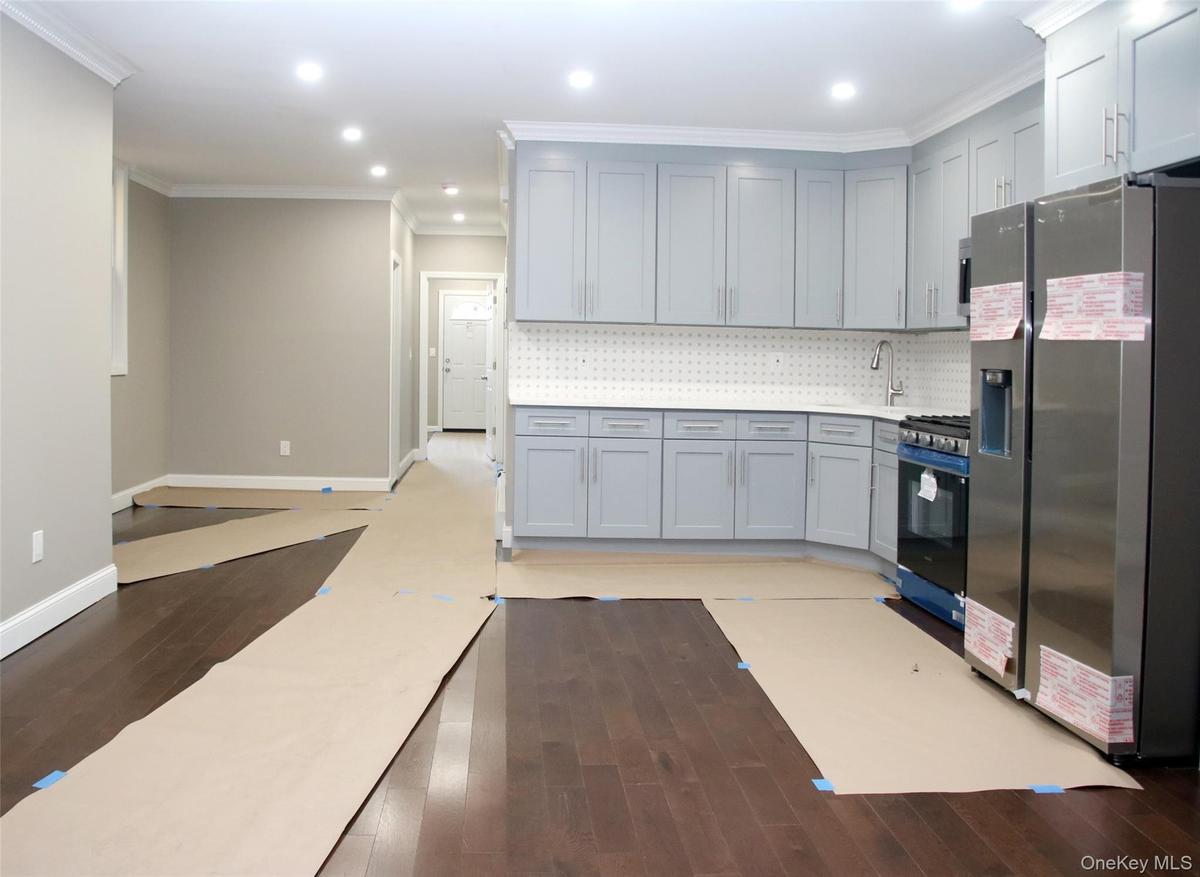 Kitchen featuring stainless steel fridge, crown molding, dark wood-style flooring, gas range oven, and tasteful backsplash