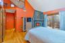 Bedroom with multiple windows, light wood-type flooring, access to exterior, a stone fireplace, and high vaulted ceiling