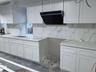 Kitchen with white cabinets, range hood, decorative backsplash, and light stone counters