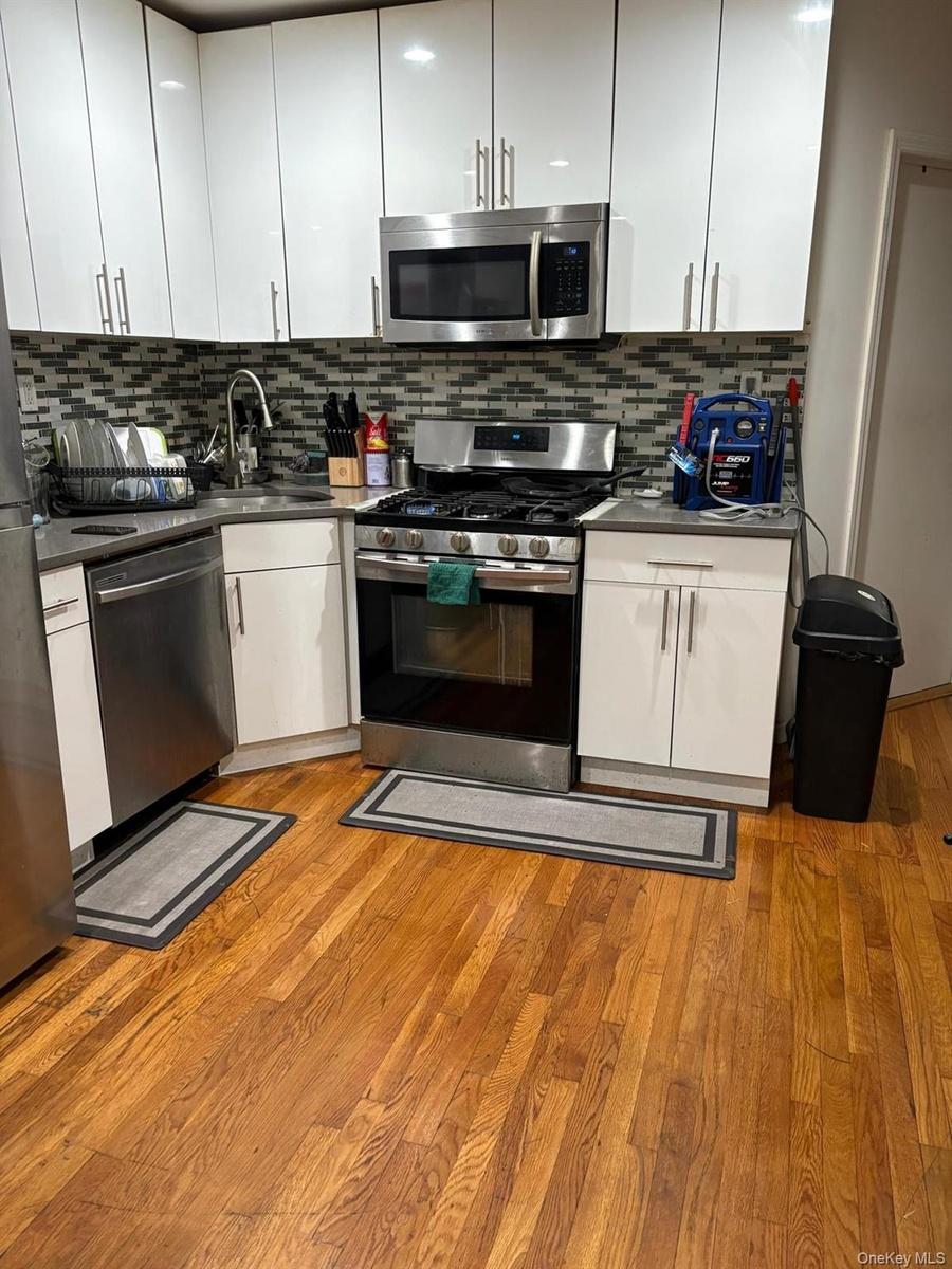 Kitchen with appliances with stainless steel finishes, white cabinetry, light wood-style floors, and tasteful backsplash