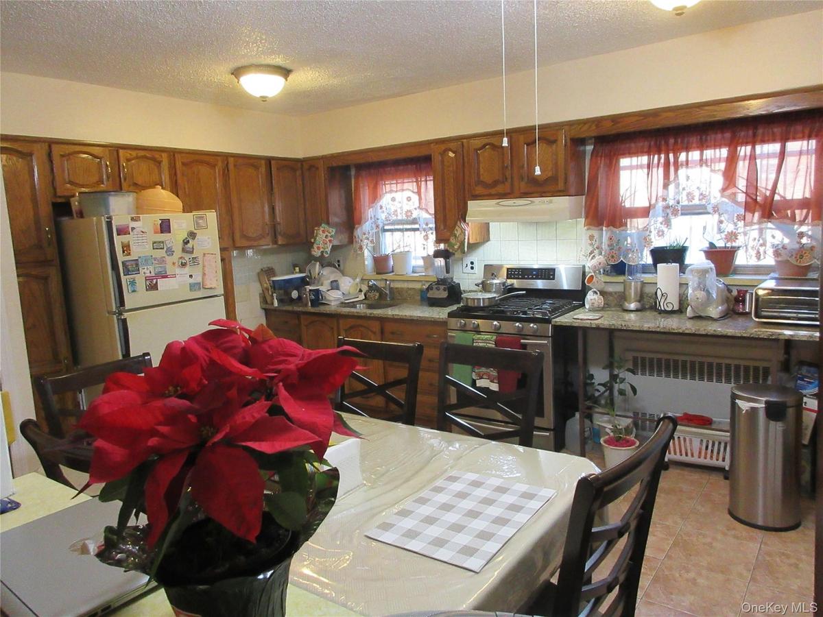 Kitchen featuring gas range, radiator heating unit, a textured ceiling, brown cabinetry, and freestanding refrigerator