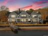 Back of house at dusk featuring a gambrel roof, a chimney, stairs, and a porch