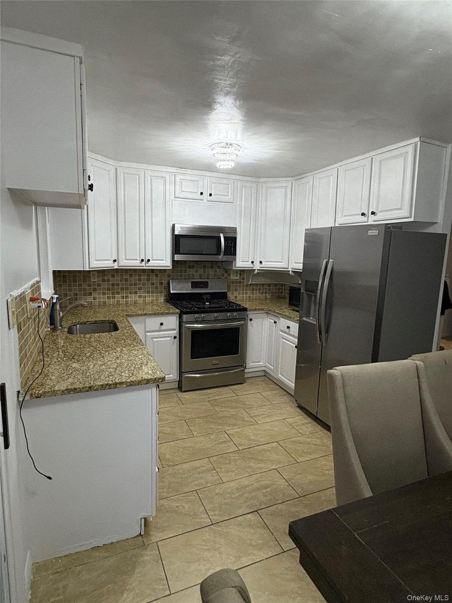 Kitchen with white cabinetry, dark stone counters, backsplash, and stainless steel appliances