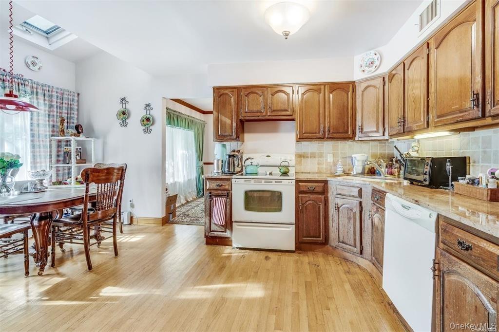 Kitchen featuring white appliances, a skylight, light wood-style flooring, backsplash, and brown cabinets