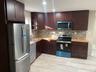 Kitchen with appliances with stainless steel finishes, dark brown cabinetry, backsplash, light wood-type flooring, and open shelves
