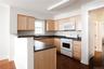Kitchen with light brown cabinets, white appliances, dark countertops, and  wood-style flooring