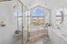 Full bath with double vanity, lofted ceiling, a garden tub, a shower stall, and plenty of natural light