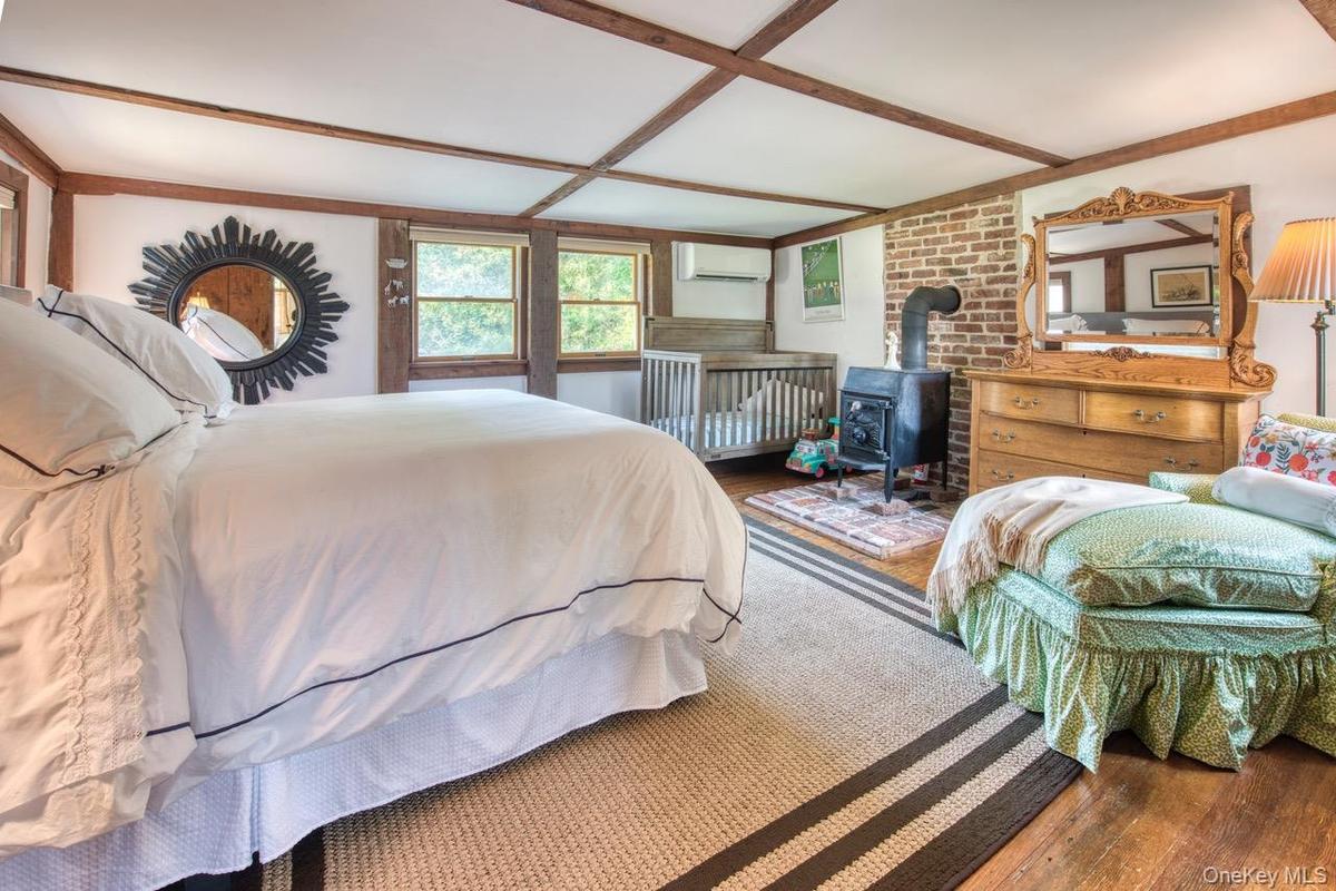 Bedroom featuring a wood stove, wood finished floors, a wall mounted air conditioner, and beamed ceiling