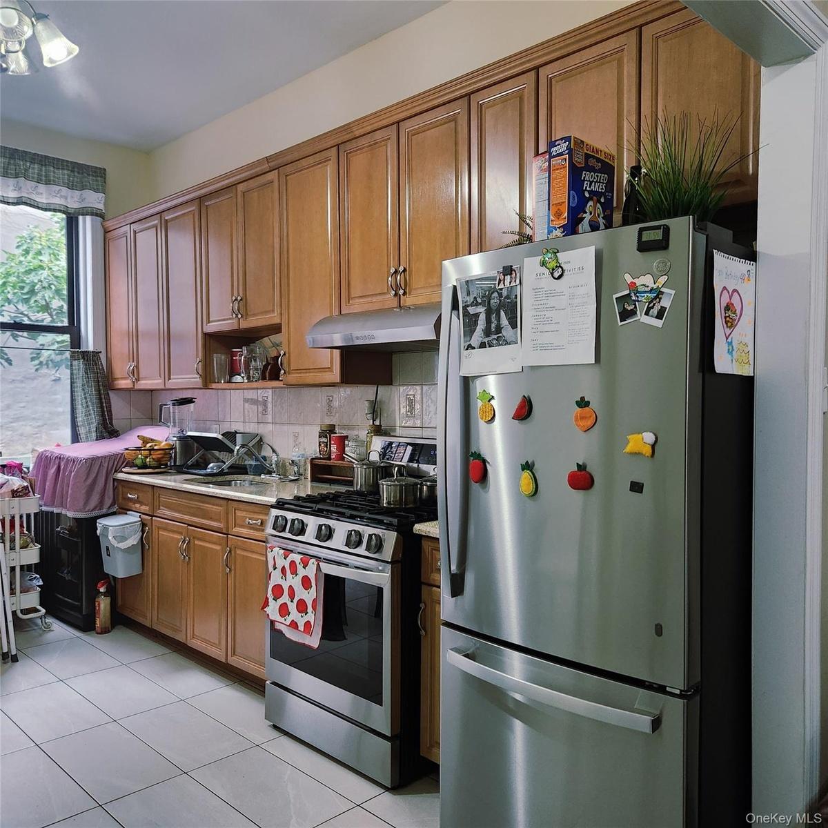Kitchen with appliances with stainless steel finishes, brown cabinetry, light tile patterned floors, light countertops, and decorative backsplash
