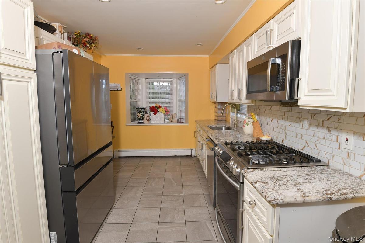 Kitchen featuring stainless steel appliances, light tile patterned flooring, decorative backsplash, light stone countertops, and white cabinetry