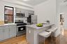 Kitchen featuring gray cabinets, appliances with stainless steel finishes, a kitchen bar, tasteful backsplash, and light stone counters