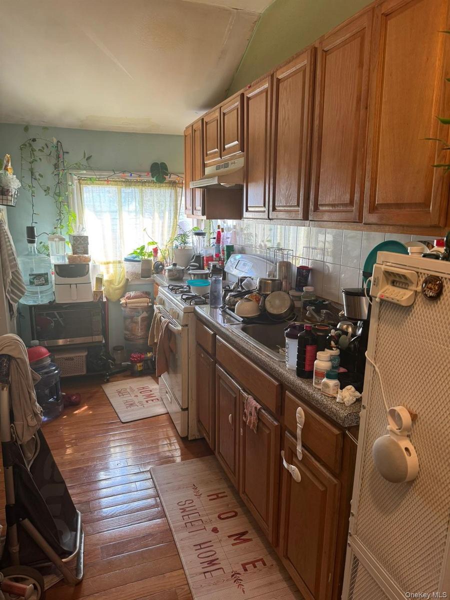 Kitchen with dark countertops, white range with gas cooktop, dark wood-style floors, brown cabinets, and under cabinet range hood