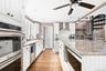 Kitchen featuring appliances with stainless steel finishes, white cabinets, light stone counters, wall chimney exhaust hood, and light wood finished f