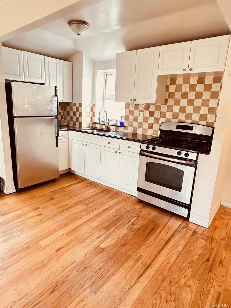 Kitchen with stainless steel appliances, white cabinets, dark countertops, backsplash, and light wood-style floors