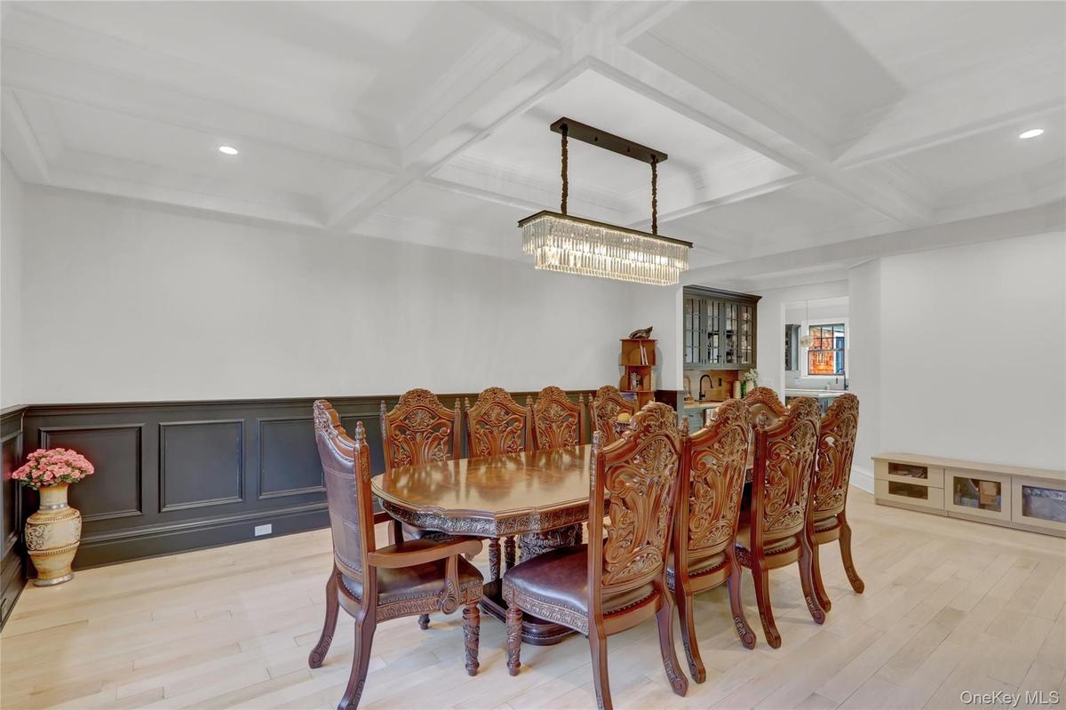 Dining area with coffered ceiling, light wood-style floors, beamed ceiling, and a decorative wall