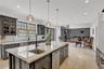 Kitchen featuring glass insert cabinets, ornamental molding, light stone counters, hanging light fixtures, and stainless steel dishwasher