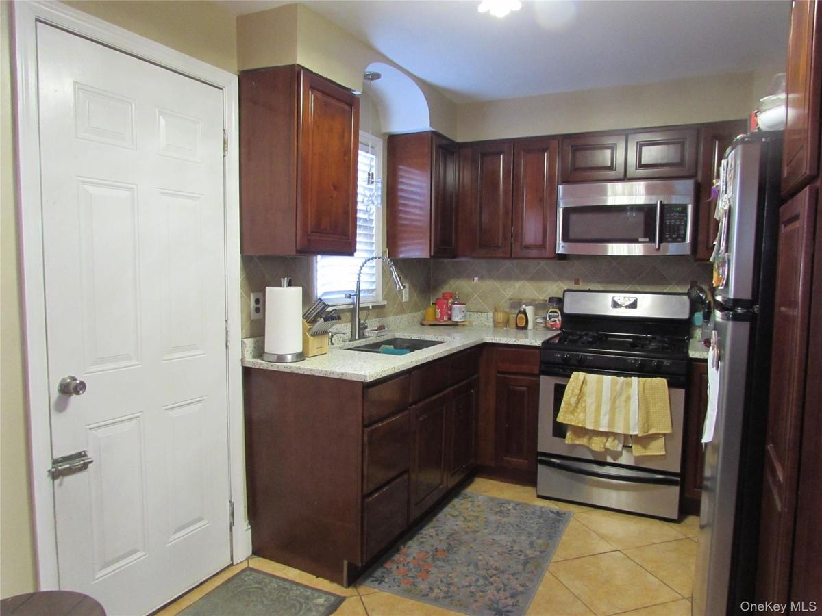 Kitchen with stainless steel appliances, decorative backsplash, light tile patterned floors, light stone countertops, and dark brown cabinets