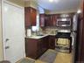 Kitchen with stainless steel appliances, decorative backsplash, light tile patterned floors, light stone countertops, and dark brown cabinets