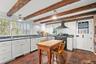 Kitchen with beam ceiling, range with two ovens, wall chimney exhaust hood, dark wood-type flooring, and dark countertops