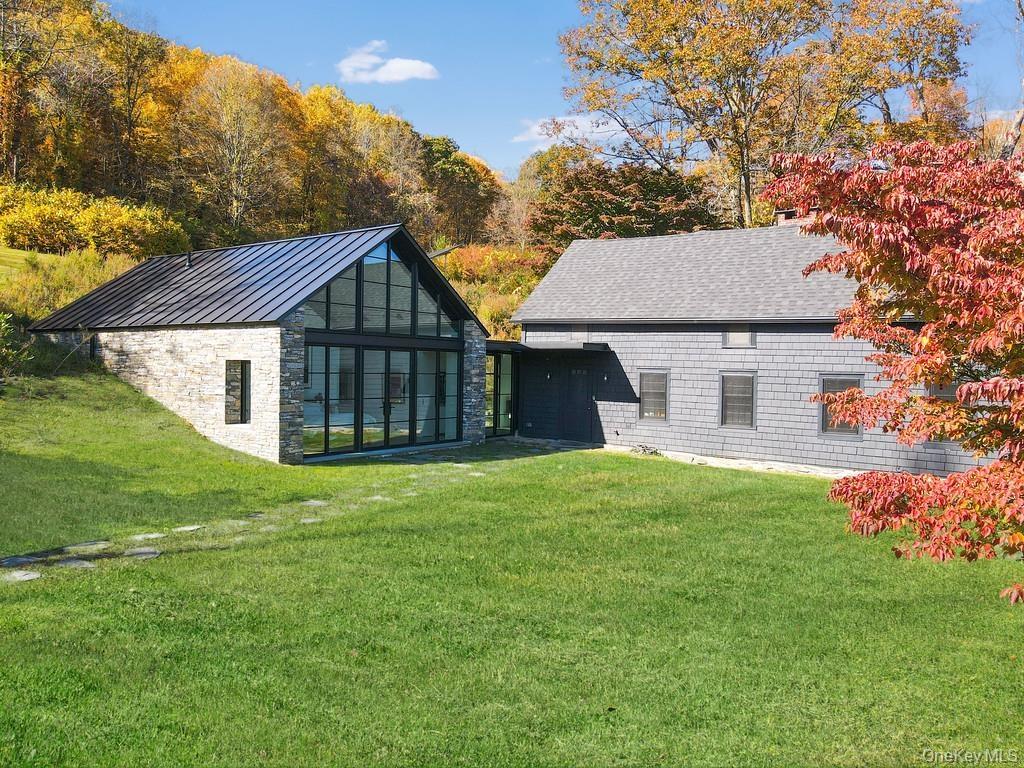 Back of house with a lawn, stone siding, a standing seam roof, and a metal roof