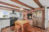 Kitchen featuring brick wall, wall chimney exhaust hood, dark wood-type flooring, range with two ovens, and white cabinets