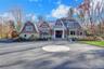 Shingle-style home featuring a gambrel roof, stone siding, and curved driveway