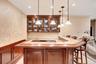 Indoor wet bar featuring glass insert cabinets, pendant lighting, light stone counters, recessed lighting, and brown cabinets