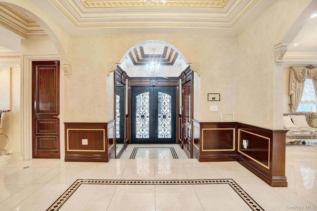 Foyer featuring arched walkways, inlaid floor details, crown molding, a wainscoted wall, and a decorative wall