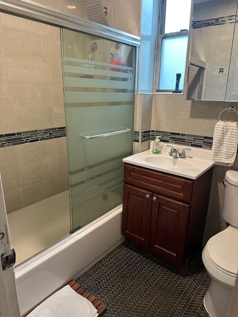 Bathroom with toilet, tile patterned floors, vanity, and enclosed tub / shower combo