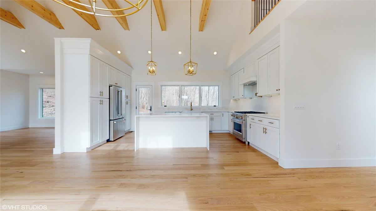 Kitchen with beam ceiling, white cabinetry, premium appliances, pendant lighting, and a kitchen island