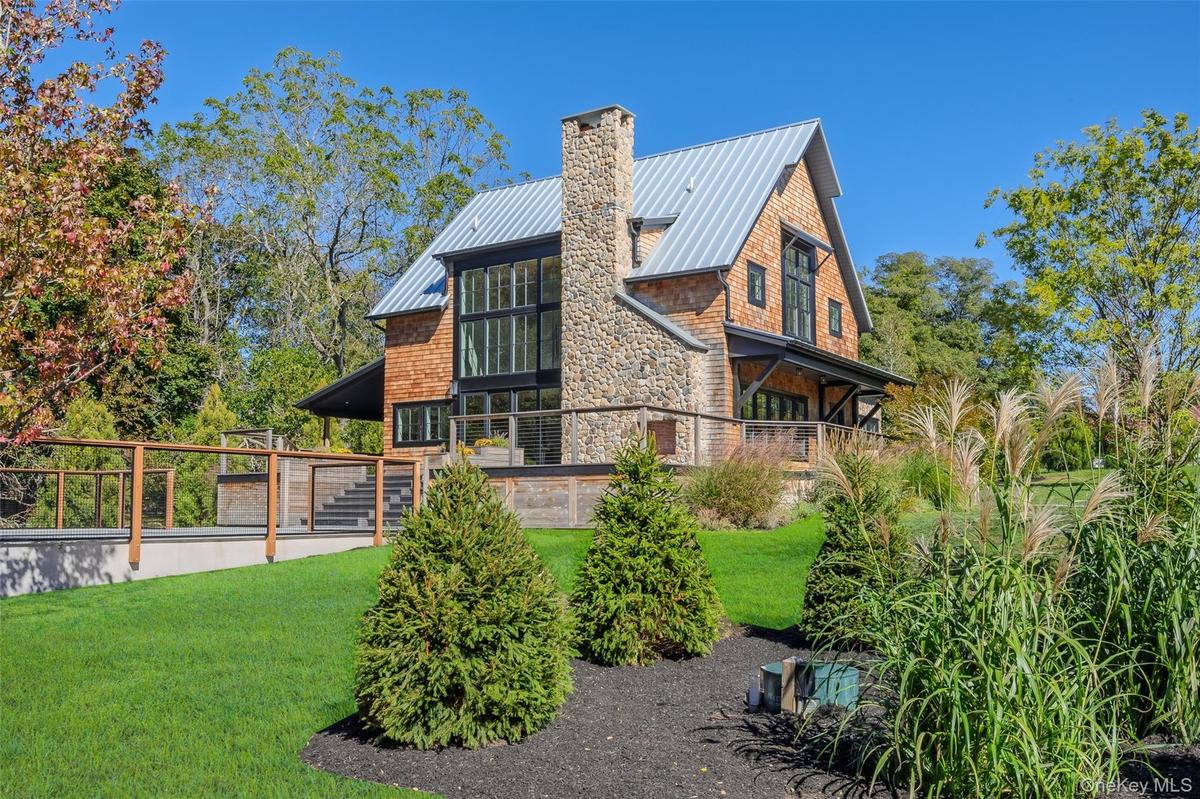 Rear view of property featuring a standing seam roof, a metal roof, a yard, a chimney, and stone siding