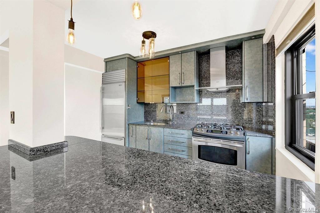 Kitchen with wall chimney range hood, stainless steel appliances, tasteful backsplash, and dark stone countertops