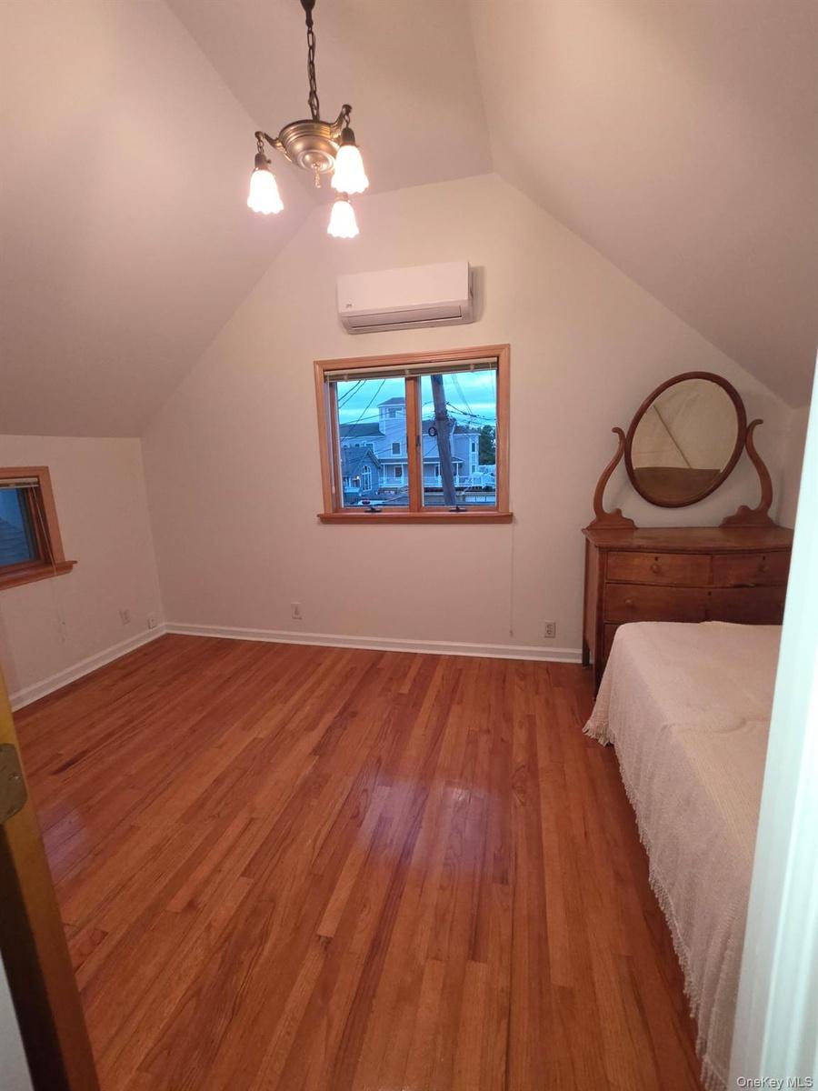 Unfurnished bedroom with light wood-style floors, lofted ceiling, a wall mounted AC, and a chandelier