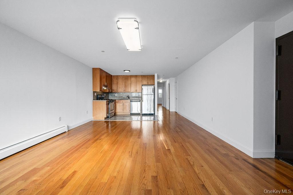 Unfurnished living room with a baseboard radiator, light wood-style flooring, and baseboards