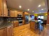 Kitchen with brown cabinetry, dark stone countertops, appliances with stainless steel finishes, glass insert cabinets, and recessed lighting