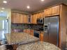 Kitchen featuring appliances with stainless steel finishes, glass insert cabinets, backsplash, brown cabinets, and dark stone countertops