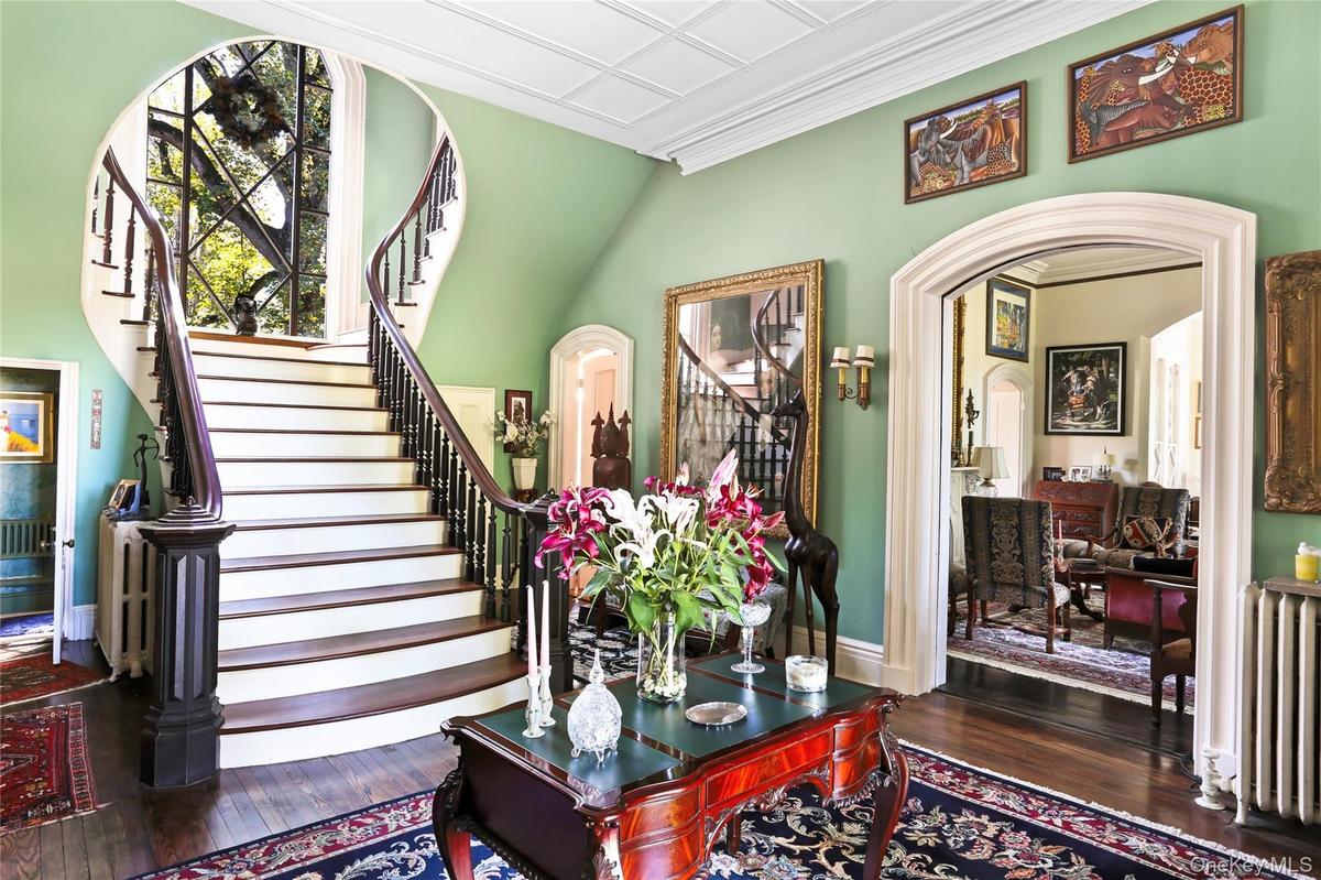 Stairway featuring radiator, hardwood / wood-style floors, arched walkways, baseboards, and ornamental molding