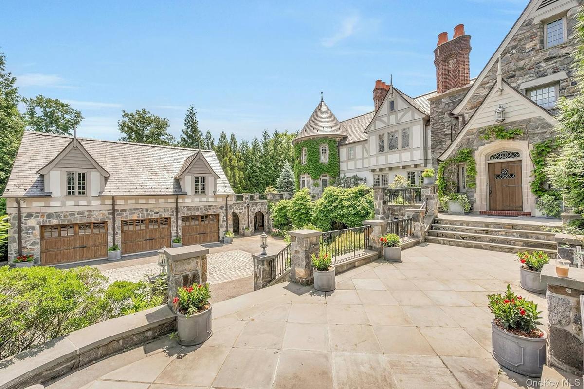 Stunning Tudor-style estate featuring stone and half-timber architecture, an ivy-covered turret, and a spacious motor court with a three car garage. T