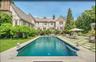This grand Tudor estate features a resort-caliber outdoor oasis centered around a sophisticated dark-bottom pool and a striking geometric stone terrac