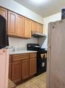 Kitchen with freestanding refrigerator, black gas range oven, brown cabinets, refrigerator, and under cabinet range hood