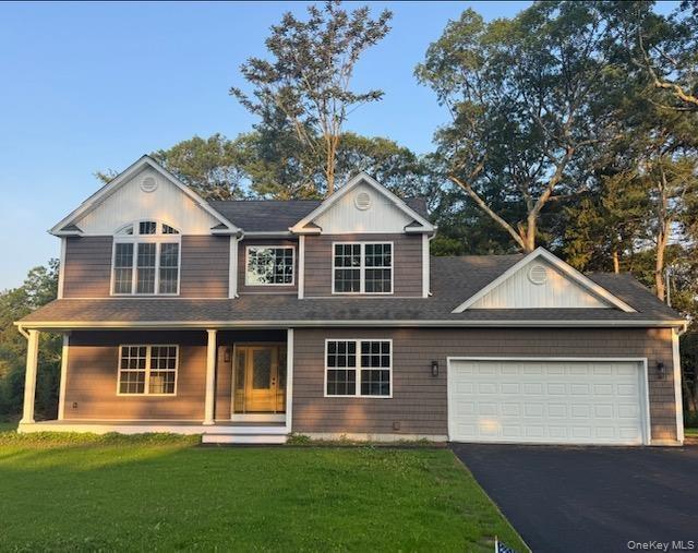 View of front of house with a front lawn, a porch, driveway, a  two car garage, and a shingled roof