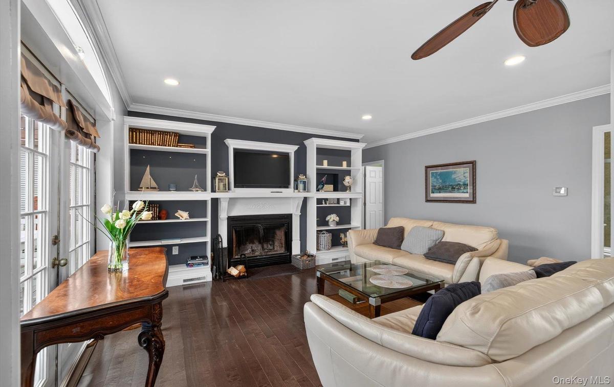 Living area with a ceiling fan, a glass covered fireplace, ornamental molding, dark wood finished floors, and built in features