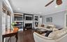 Living area with a ceiling fan, a glass covered fireplace, ornamental molding, dark wood finished floors, and built in features