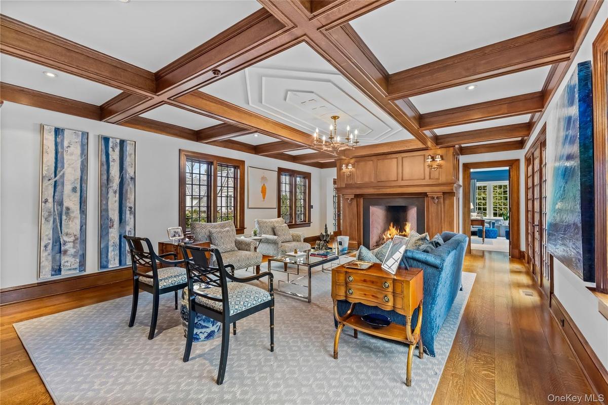 Living room with light wood-oak flooring, a fireplace, coffered ceiling, and suspended lighting.